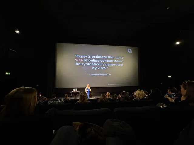 Speaker stands in front of the audience, the screen on her back reads “Experts estimate that up to 90% of online content could be synthetically generated by 2026”